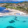 Una baia con acqua turchese e spiaggia di sabbia bianca circondata da vegetazione e case.