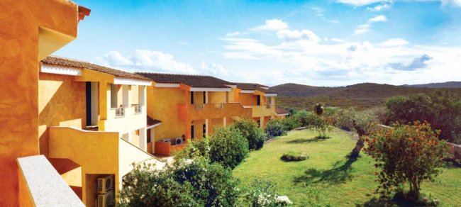 Edificio color ocra con giardino, immerso in un paesaggio naturale sotto un cielo azzurro.
