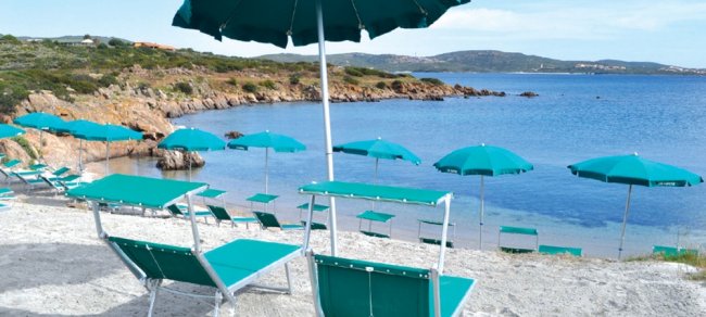 Spiaggia con ombrelloni e lettini verdi, vicino al mare e rocce.