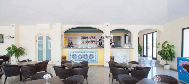 Interno di un bar con tavolini e sedie, decorazioni luminose e piante.