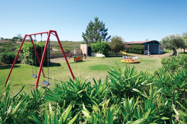 Un parco giochi con altalene rosse e giostre su prato verde.