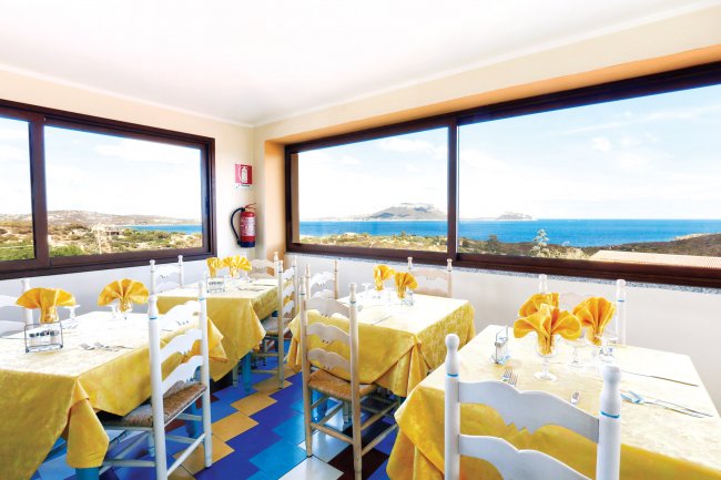 Sala da pranzo con tavoli apparecchiati, finestroni con vista sul mare.