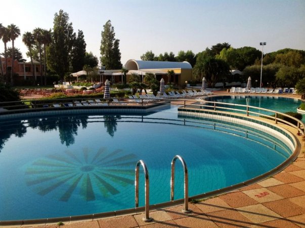 Piscina con gradini e ombrelloni, contornata da alberi.