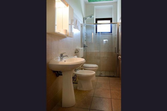 Un bagno con lavabo, bidet e cabina doccia. Pareti beige e finestra in alto.
