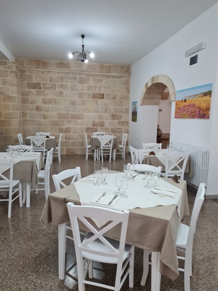 Sala ristorante con pareti in pietra, tavoli apparecchiati e sedie bianche.
