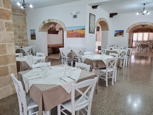 Interno di un ristorante con tavoli apparecchiati, sedie bianche e decorazioni alle pareti.