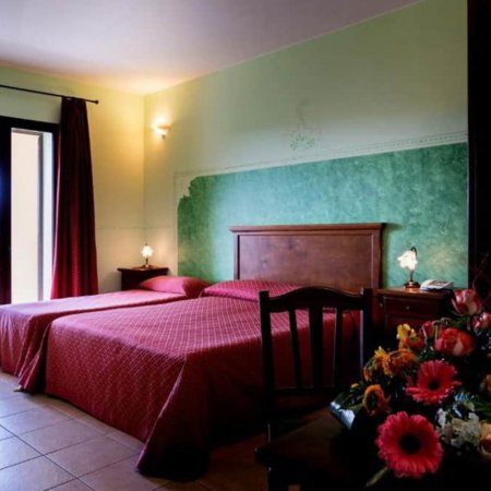 Due letti singoli con copriletti rossi, parete verde e fiori su un tavolo.