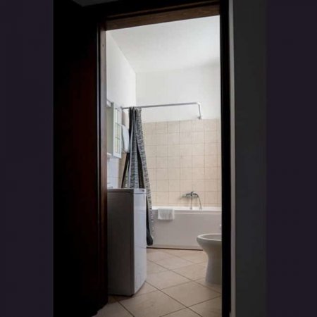 Bagno con vasca, tende e lavatrice, piastrelle beige.