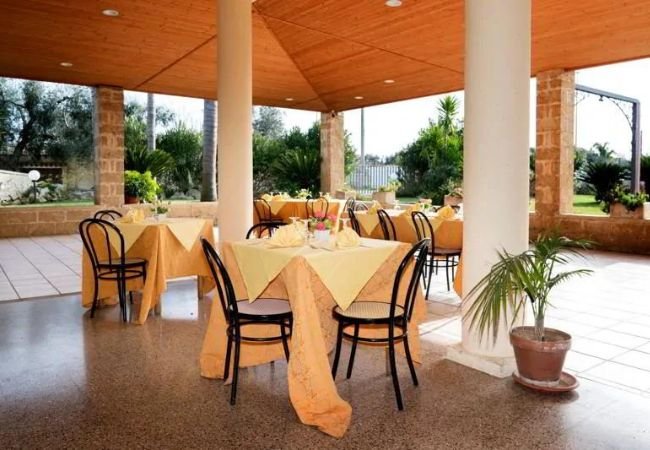 Ristorante all'aperto con colonne, tavoli apparecchiati e vista sul giardino.