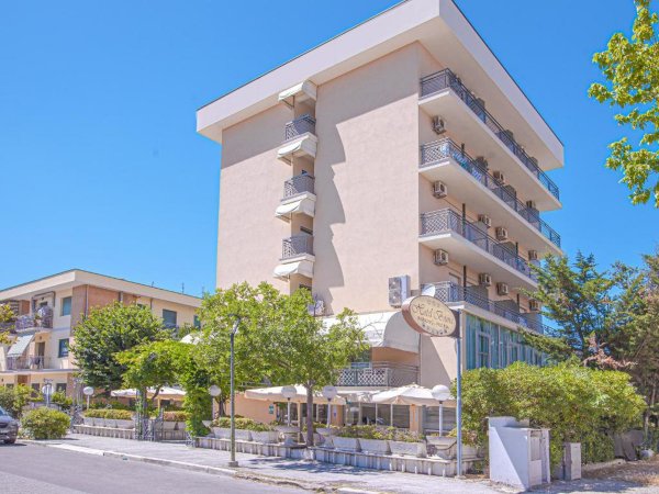 Edificio a più piani con balconi, circondato da alberi in una giornata di sole.