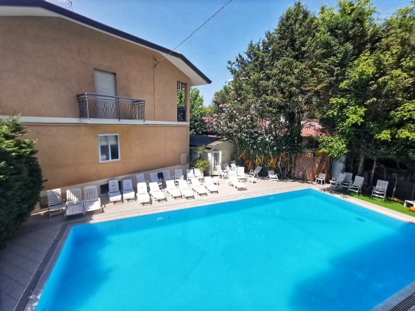 Vista della piscina circondata da lettini bianchi e alberi rigogliosi.
