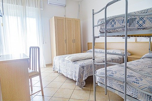 Camera con letto matrimoniale e letti a castello, tende bianche e mobilio chiaro.