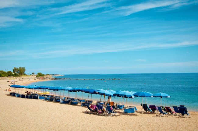 Spiaggia con lettini e ombrelloni blu.