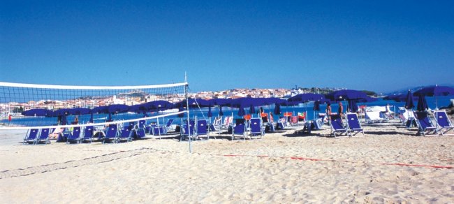 Una spiaggia con sedie a sdraio blu, ombrelloni e una rete da pallavolo di fronte al mare.