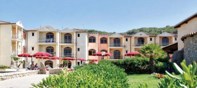 Complesso residenziale con balconi e ombrelloni rossi, circondato da giardini curati.
