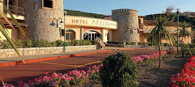 Ingresso dell'Hotel Posada, con facciata in pietra e aiuole fiorite lungo il vialetto.