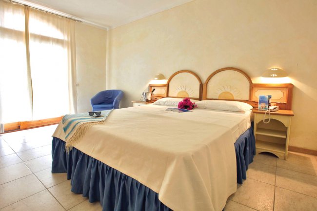 Camera d'albergo con letto matrimoniale, comodini e una poltrona blu.