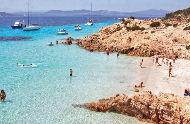 Spiaggia rocciosa con acqua cristallina e persone che nuotano e si rilassano.