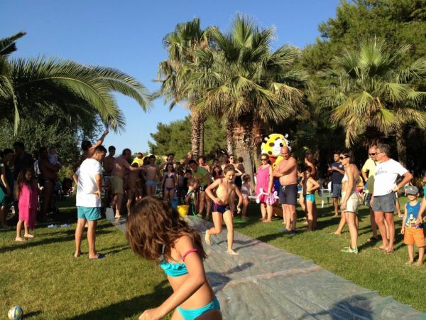 Bambini giocano su un telo scivoloso sotto le palme.