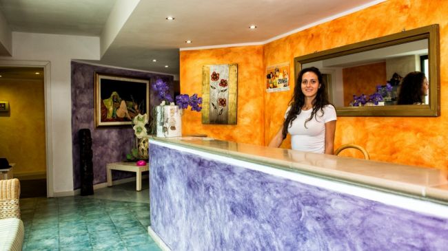 Reception con arredamento colorato e donna sorridente dietro il bancone.