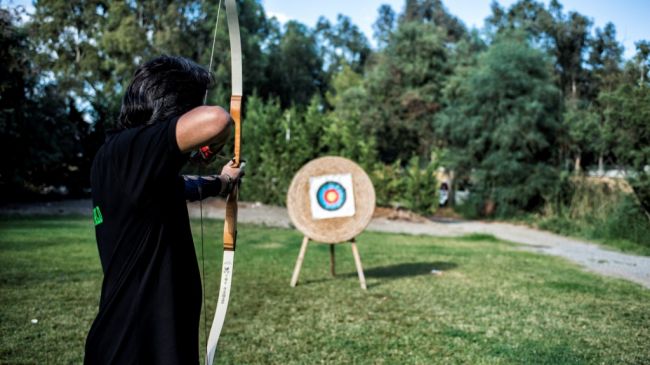 Persona che scocca una freccia verso un bersaglio in un campo.
