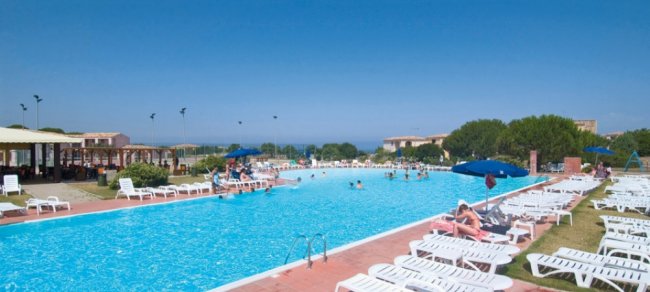 Piscina all'aperto con sdraio bianche e ombrelloni blu.