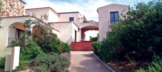 Una villa bianca con giardino e vialetto d'ingresso.