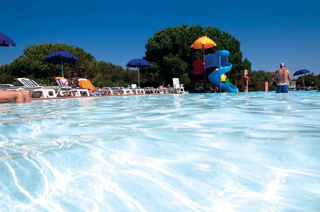 Una piscina con scivolo e sdraio.