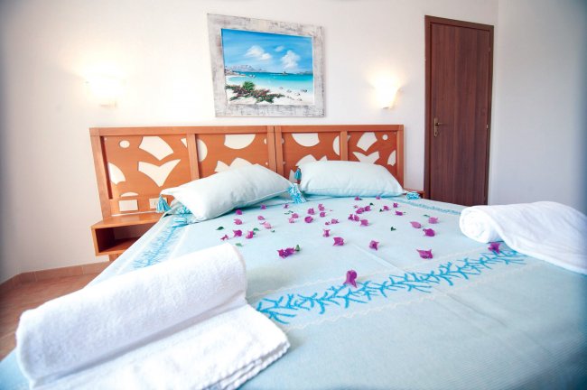 Letto con cuscini azzurri e petali rosa.