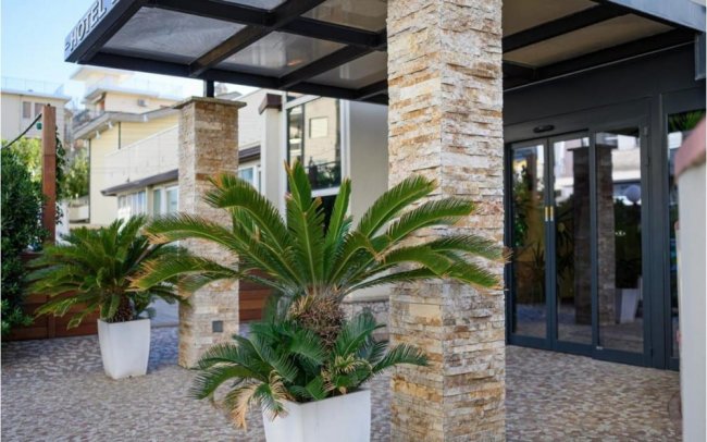 Ingresso hotel con piante in vaso e colonne.