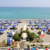 Spiaggia con ombrelloni blu, sentiero centrale e mare calmo in lontananza.