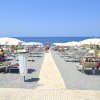Spiaggia con sedie a sdraio e ombrelloni bianchi, mare sullo sfondo.