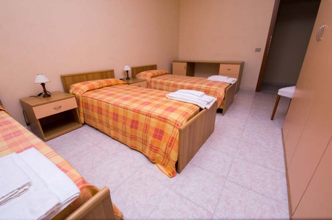 Camera con tre letti singoli e comodini.