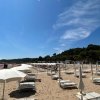 Lettini e ombrelloni bianchi su una spiaggia sabbiosa sotto un cielo blu.