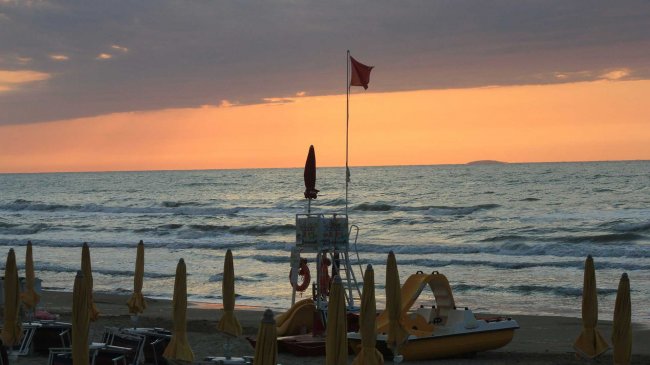 Spiaggia al tramonto con ombrelloni e barca.