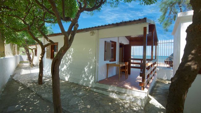 Casetta bianca con veranda e alberi intorno.