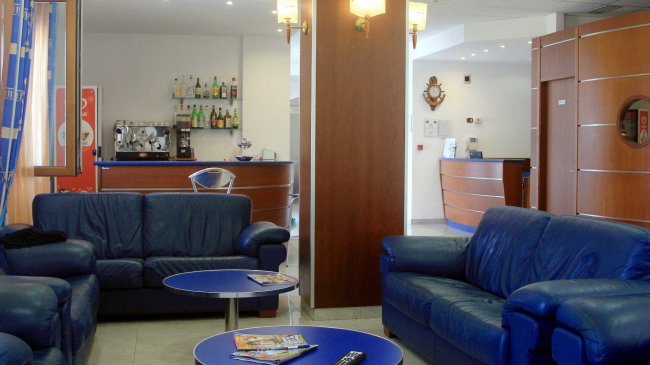 Lobby con divani blu e un bar sullo sfondo.