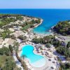 Vista aerea di resort con piscina e baie affacciate su mare azzurro.