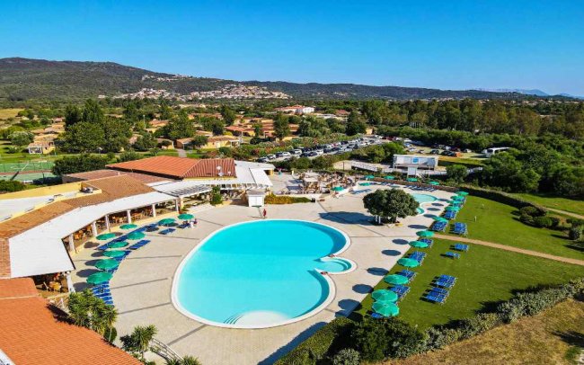 Piscina esterna con lettini, ombrelloni e vista su colline e case.